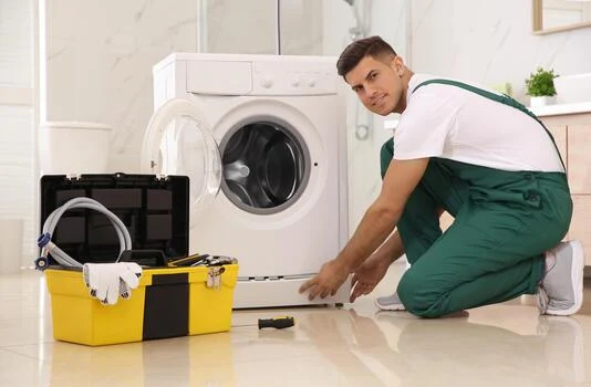 Appliance technician in green overalls inspecting a washing machine