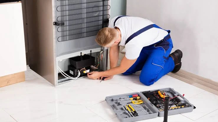 Technician diagnosing the compressor area at the back of a refrigerator